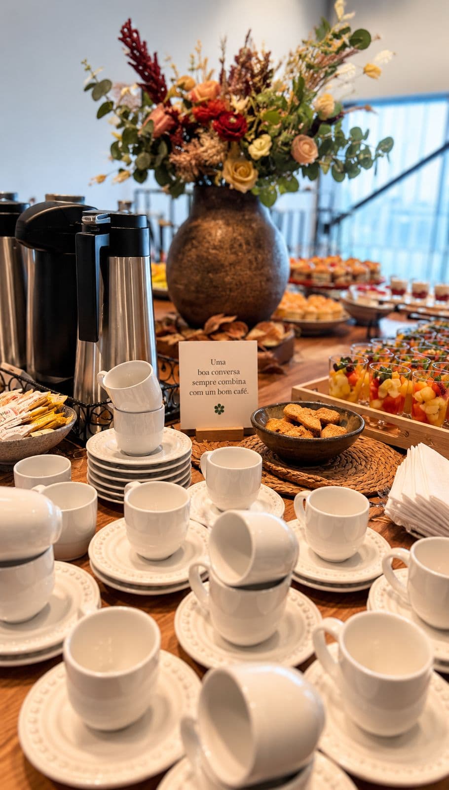 Mesa de café da manhã com xícaras brancas e arranjo floral ao fundo